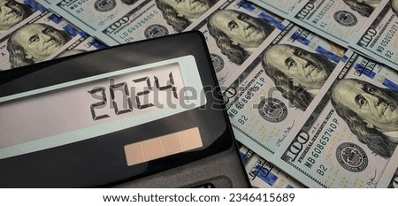 New year 2024. Money is laid out in rows on the table and a calculator. US dollar bills in the background. Photo to illustrate finance and economics concepts
