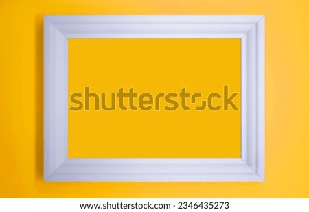 Photo of white blank frame hanging on yellow wall.