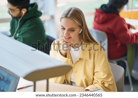 Happy girl student using laptop looking at computer sitting at desk in university college campus classroom hybrid learning online,watching webinar class, elearning or remote working in coworking. Royalty-Free Stock Photo #2346440565