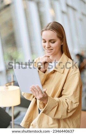 Happy girl student using pad looking at digital tablet. Young woman holding tab computer modern tech device standing in university campus, coworking office space. Vertical shot