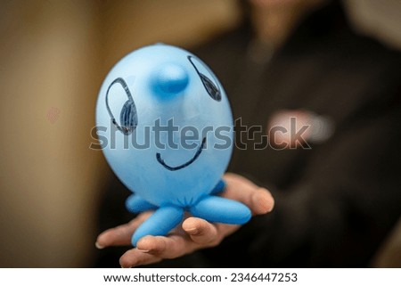 A Young woman is holding a blue glove balloon with a smile on it in the camera. This is a little trick for working with kids in the health system to make them happy.