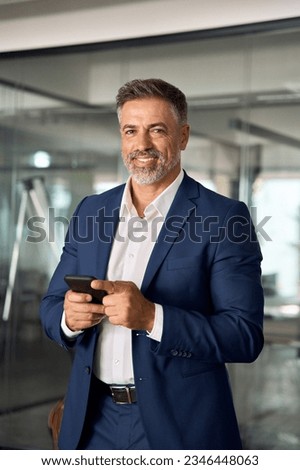 Vertical photo of mature Latin businessman holding smartphone in office. Middle aged manager using cell phone mobile app. Digital technology application and solutions for business success development. Royalty-Free Stock Photo #2346448063