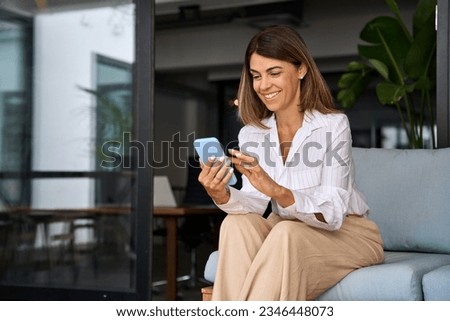 European businesswoman CEO holding smartphone using fintech application sitting on sofa in modern office. Smiling Latin Hispanic mature adult professional business woman using mobile phone cellphone.  Royalty-Free Stock Photo #2346448073