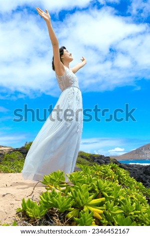 Teen girl in white dress raising arms in praise outdoors on Hawaiian coast