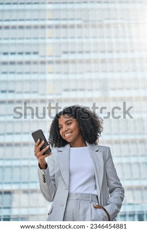 Happy young African American business woman using cell phone outdoor. Smiling lady professional holding smartphone standing at city street building looking at mobile working outside office, vertical. Royalty-Free Stock Photo #2346454881