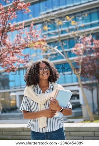 Happy pretty female African American student walking outside applying university foreign program. Smiling cheerful girl model wearing glasses, holding notebooks looking away outdoors, vertical. Royalty-Free Stock Photo #2346454889