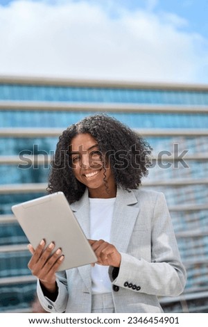 Happy young African American business woman holding digital tablet standing in city street, smiling busy sales professional ethnic lady corporate leader working outside office. Vertical portrait Royalty-Free Stock Photo #2346454901