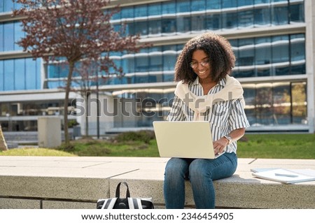 Young happy ethnic African American girl student using laptop computer learning sitting in university garden park, studying online digital remote class or elearning on pc device outdoors.