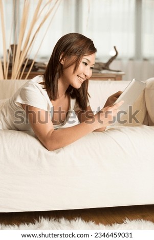 Portrait of a happy Chinese woman sitting on sofa using Digital Tablet