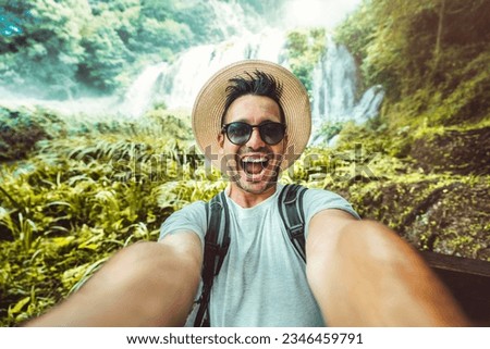 Happy traveler man with backpack taking selfie picture in the forest - Travel blogger taking self portrait with smart mobile phone device outside - Life style and technology concept