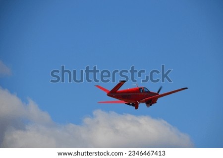 A photo of a red vintage V-tail airplane taken as it takes off and flies away.