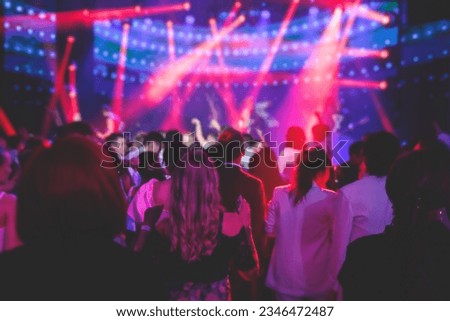 A crowded concert hall arena with scene stage lights with musicians band on a stage at the venue, rock show performance, with concert-goers attendees, audience on dance floor during concert festival
 Royalty-Free Stock Photo #2346472487