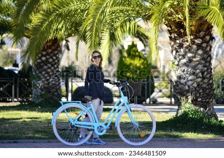 Smiling woman with sunglasses and vintage bicycle in spring,autumn weather in exotic country with palm trees