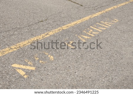 no parking caption print text writing in yellow below line on pavement, worn and faded, shot on angle going diagonal Royalty-Free Stock Photo #2346491225