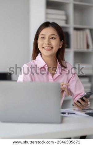 Asian businesswoman holding smartphone searching for information through website, online, surfing the internet with graph paper Work chart lying on the desk in the office