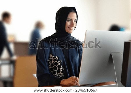 Real Arab woman at office wearing Abaya Hijab with workmate colleagues employees people around. Middle East, UAE, Saudi Arabia, Qatar, Bahrain, Oman, Kuwait concept mock up for business or school Royalty-Free Stock Photo #2346510667