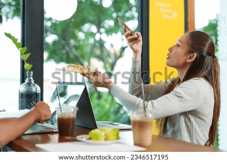 Beautiful Asian woman using a smartphone take pictures of croissants placed on a wooden tray to prepare for the social media of the store recommend to customers to see and put it in online menu