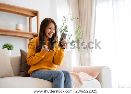 Happy young asian woman relax on comfortable couch at home texting messaging on smartphone, smiling girl use cellphone, chatting online message, shopping online from home Royalty-Free Stock Photo #2346522325
