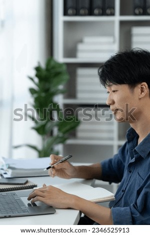 Young businessman, asian office worker sitting working on laptop computer in office data research concept note taking online learning