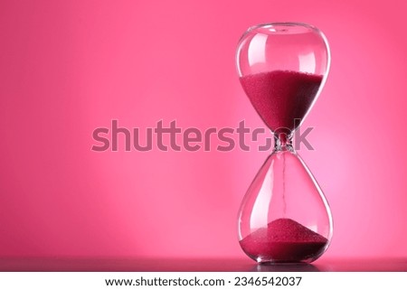 Hourglass with flowing sand on table against pink background, space for text Royalty-Free Stock Photo #2346542037