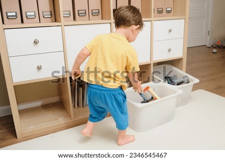 The child is putting the toys back in the box after playing. Kid toddler boy aged two years Royalty-Free Stock Photo #2346545467