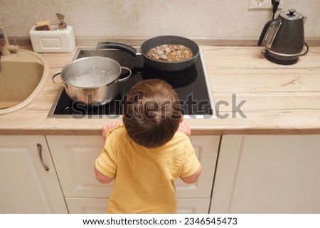 Baby reaches for the hot stove with a pot of boiling water. Child safety issues in the home room. Kid aged two years Royalty-Free Stock Photo #2346545473