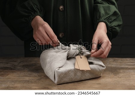 Furoshiki technique. Woman wrapping gift in fabric at wooden table, closeup Royalty-Free Stock Photo #2346545667