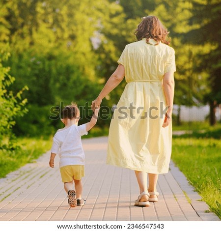 The woman walks down the path with her baby. Child holds onto his mother's hand tightly, feeling safe in her embrace. Kid aged about two years (one year eleven months) Royalty-Free Stock Photo #2346547543