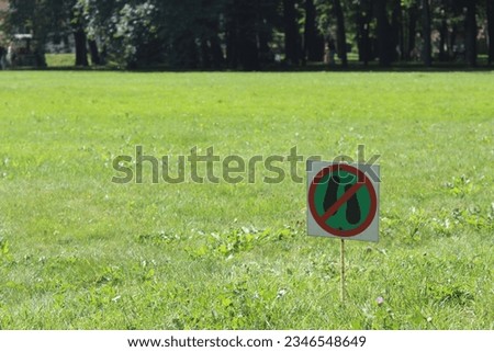 A sign of green color prohibiting walking on the territory of the meadow against the background of green grass. A sign standing on the grass and forbidding a person to stand on the grass.
