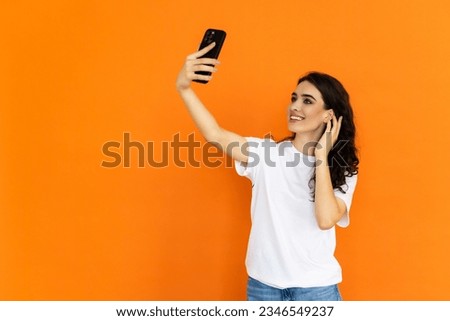 Smiling blond woman taking selfie against orange background