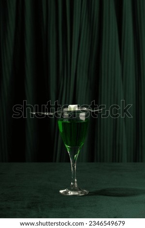 Green cocktail with sugar cube on silver spoon on dark green background