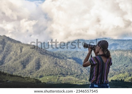 Cheerful young female photographer taking pictures with digital camera on mountains Travel and active living and tourism concept.