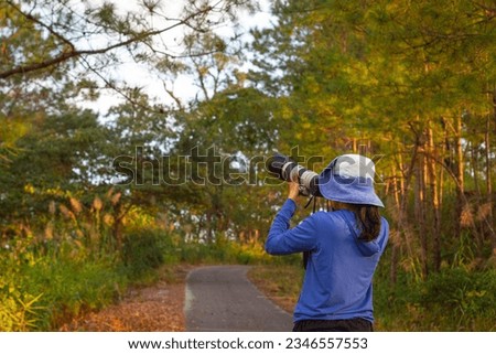 Cheerful female photographer stands with a car on the side of the road taking a picture with a digital camera in the mountains. Travel and active living and tourism concept.