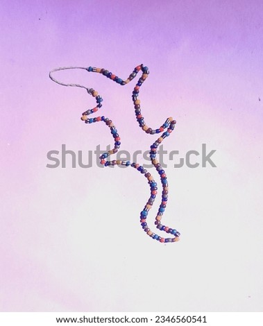 Image of a lizard animal made of a necklace of colorful beads on a light purple floor.