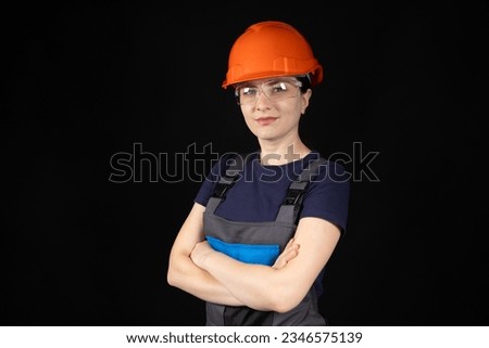 A woman in a protective helmet, glasses and overalls on a black background with space for text. Royalty-Free Stock Photo #2346575139