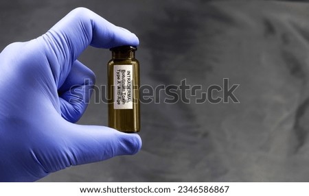 Hand with blue glove holding a bottle of Botulinum toxin type A for intradermal injection on a dark background. Royalty-Free Stock Photo #2346586867