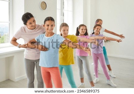 Female friendly choreographer helping her students girls in doing a dance exercises in studio. Kids doing dance workout. Happy children training in a group choreography class, learning modern dances.