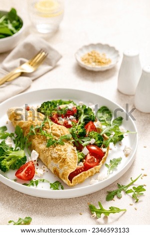 Omelette stuffed with tomato, broccoli, feta cheese and fresh green leaves of arugula and spinach. Healthy diet food, breakfast Royalty-Free Stock Photo #2346593133