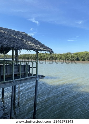 a landscape photo consisting of a dining hut, a flowing river, green trees on the other side and a clear blue sky