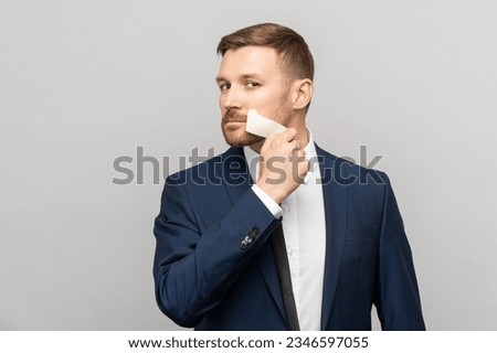 Office worker in suit peeling off tape from mouth on studio gray background looking at camera. Total subordination at work, lack of one's own opinion, prohibition of statements, censorship concept.  Royalty-Free Stock Photo #2346597055