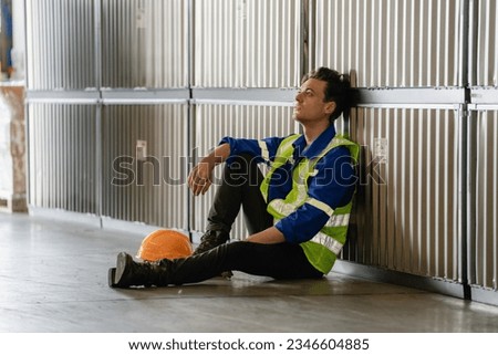 Tired sadly and bored manual worker sitting on the floor in a warehouse