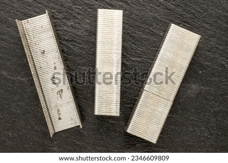 Several metal stapler staples on slate stone, macro, top view.