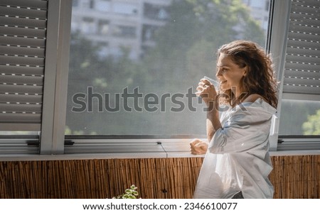 Young smiling caucasian woman in a white shirt standing on the balcony in the morning and meeting a new day Royalty-Free Stock Photo #2346610077