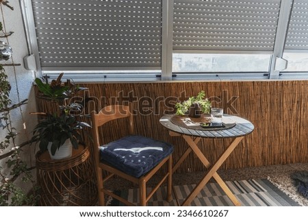 Summer loggia with roller shutters, a chair and a table with a potted plant and a glass of water Royalty-Free Stock Photo #2346610267