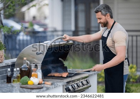 Barbecue concept. Middle aged hispanic man in apron for barbecue. Roasting and grilling food. Roasting meat outdoors. Barbecue and grill. Cooking meat in backyard.