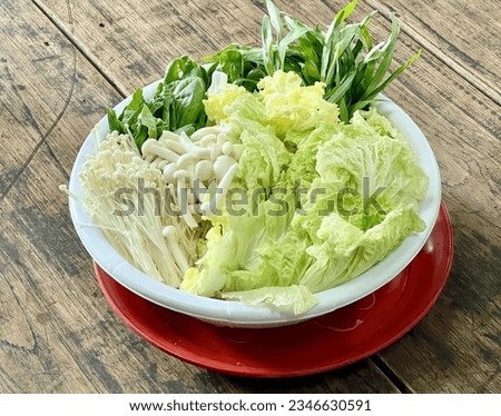 a photography of a bowl of lettuce and other vegetables on a table, there is a bowl of lettuce and other vegetables on a red plate.