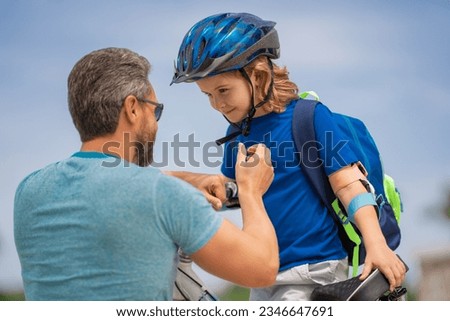 Fathers day. Father teaching son ride a bicycle. Father helping his son to wear a cycling helmet. Child in safety helmet. Father support child. Fathers love. Sporty kids.
