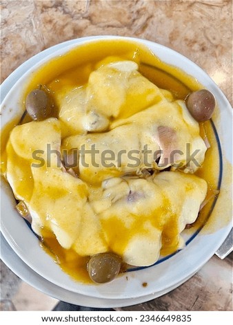 A Portuguese dish called Pica with ham, steak and sausage under melted cheese in a sauce accompany with few olives