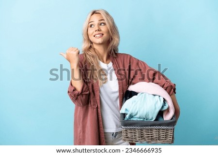 Young Russian woman holding a clothes basket isolated on blue background pointing to the side to present a product