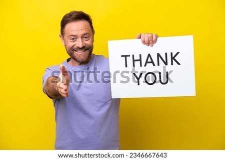 Middle age caucasian man isolated on yellow background holding a placard with text THANK YOU making a deal